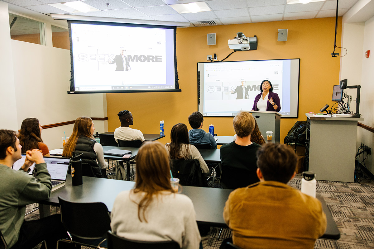 professor teaching a class with screens behind her